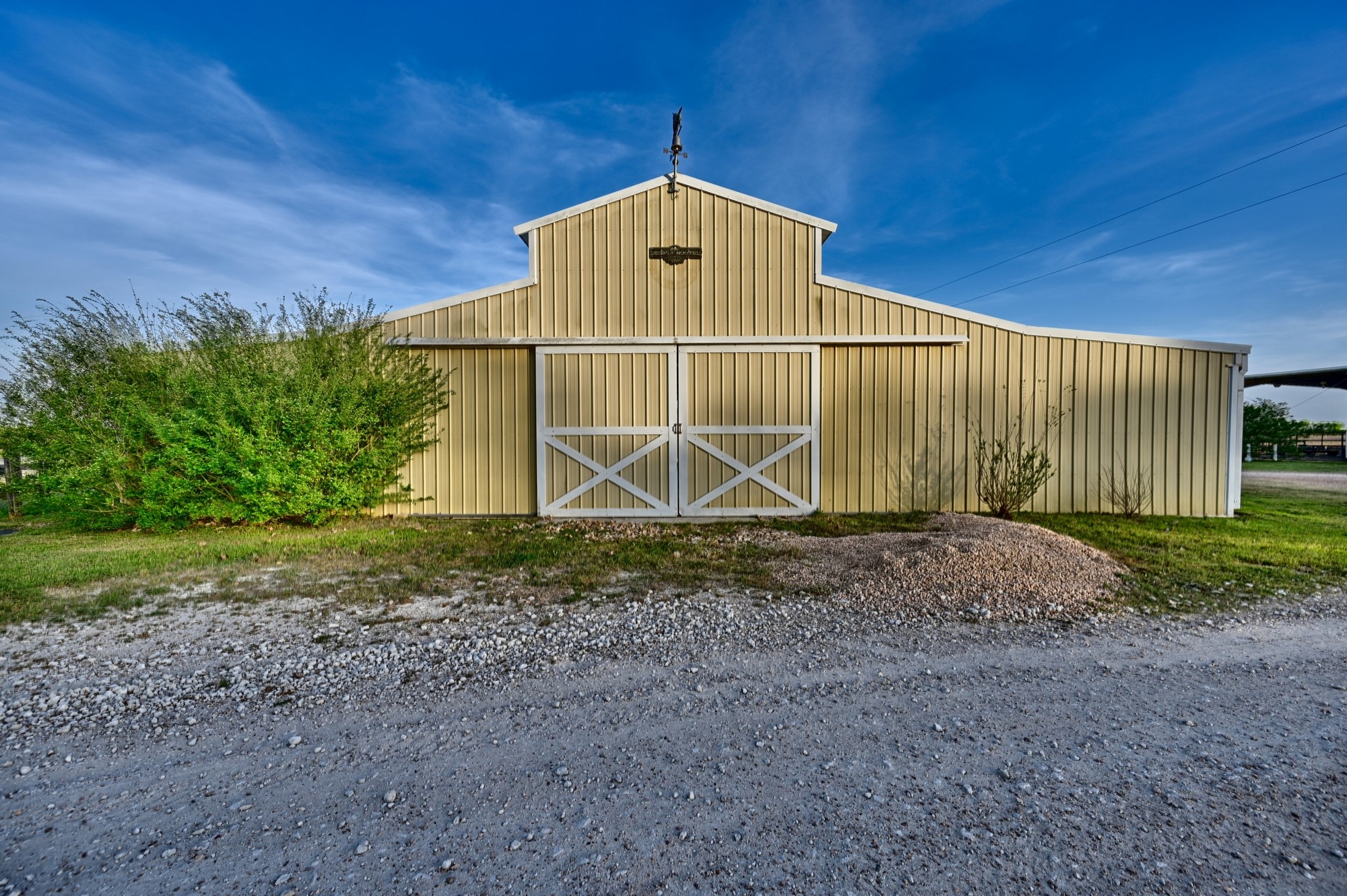 5255 Ganske Road Burton, TX 77835 - Photo 24 of 46 Beautiful barn with large sliding doors, set against a clear blue sky. It's surrounded by greenery and gravel, ideal for rural living or agricultural use.