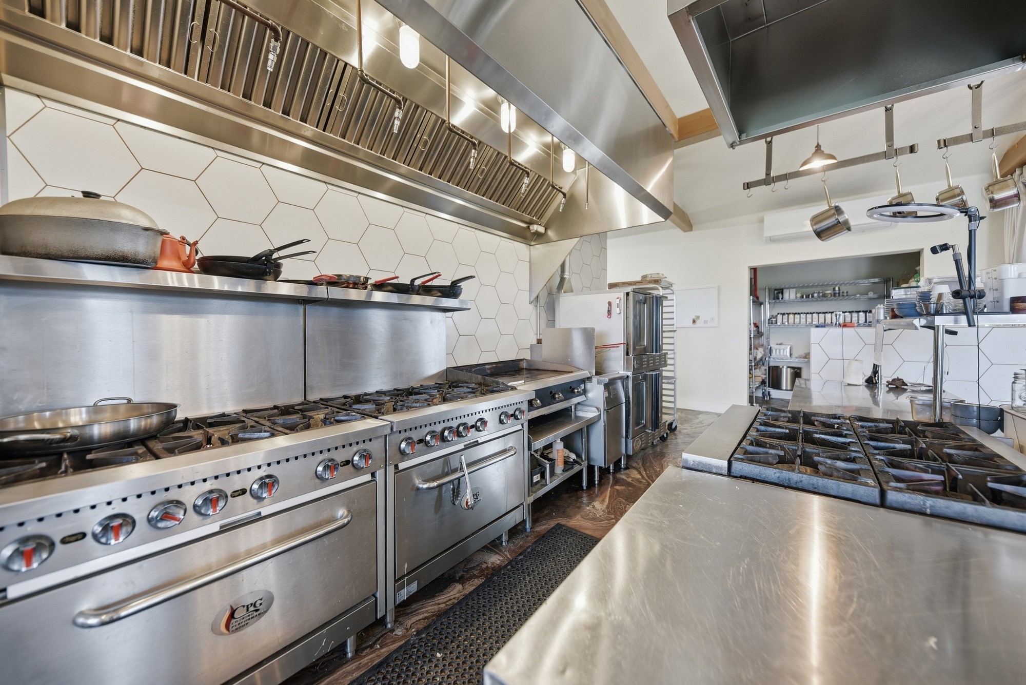 5255 Ganske Road Burton, TX 77835 - Photo 32 of 46 Professional-grade kitchen with multiple stoves and ovens, stainless steel surfaces, and a sleek hexagonal tile backsplash. Ideal for culinary enthusiasts or those needing a commercial setup.
