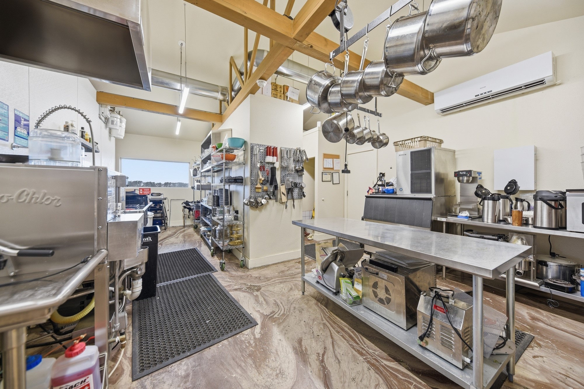 5255 Ganske Road Burton, TX 77835 - Photo 35 of 46 Well-equipped commercial kitchen with stainless steel counters, hanging pots, open shelving, and ample natural light. It's designed for efficiency and functionality, ideal for a home buyer interested in culinary endeavors or catering needs.