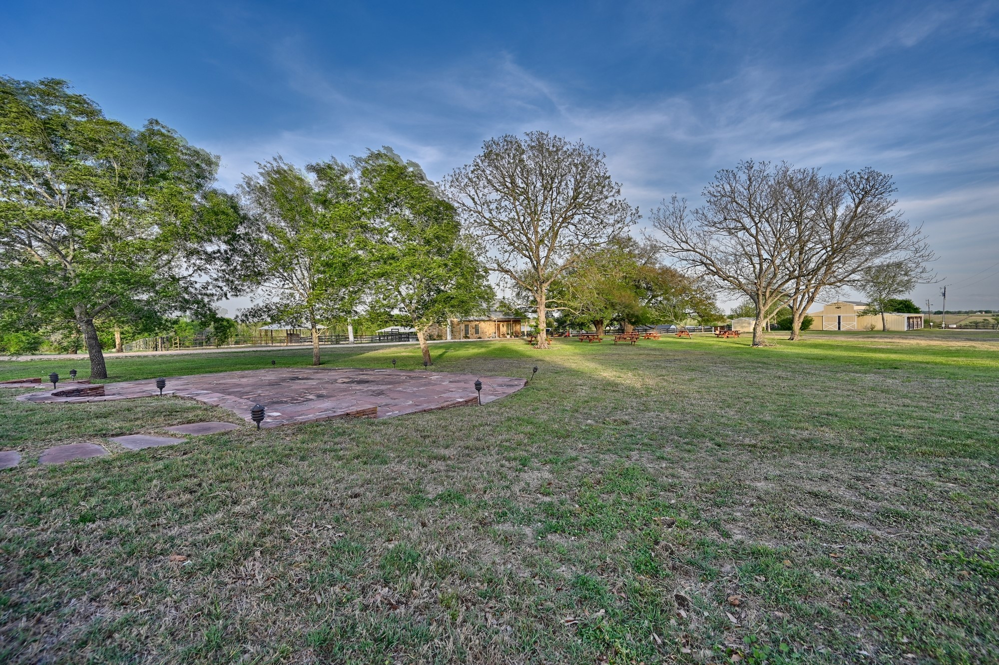 5255 Ganske Road Burton, TX 77835 - Photo 37 of 46 Spacious lawn with mature trees, a paved patio area, and ample green lawn, offering a serene outdoor setting. Perfect for events and live music.