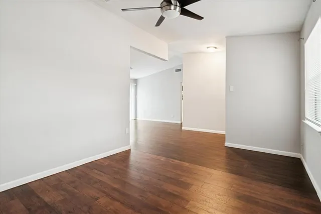 an empty room with wooden floor fan and windows