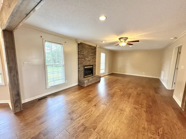 an empty room with wooden floor fireplace and windows