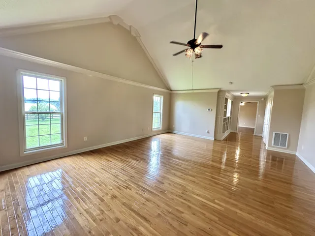 an empty room with wooden floor chandelier fan and windows