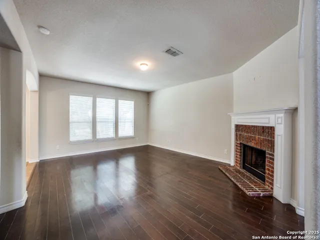 an empty room with wooden floor fireplace and windows