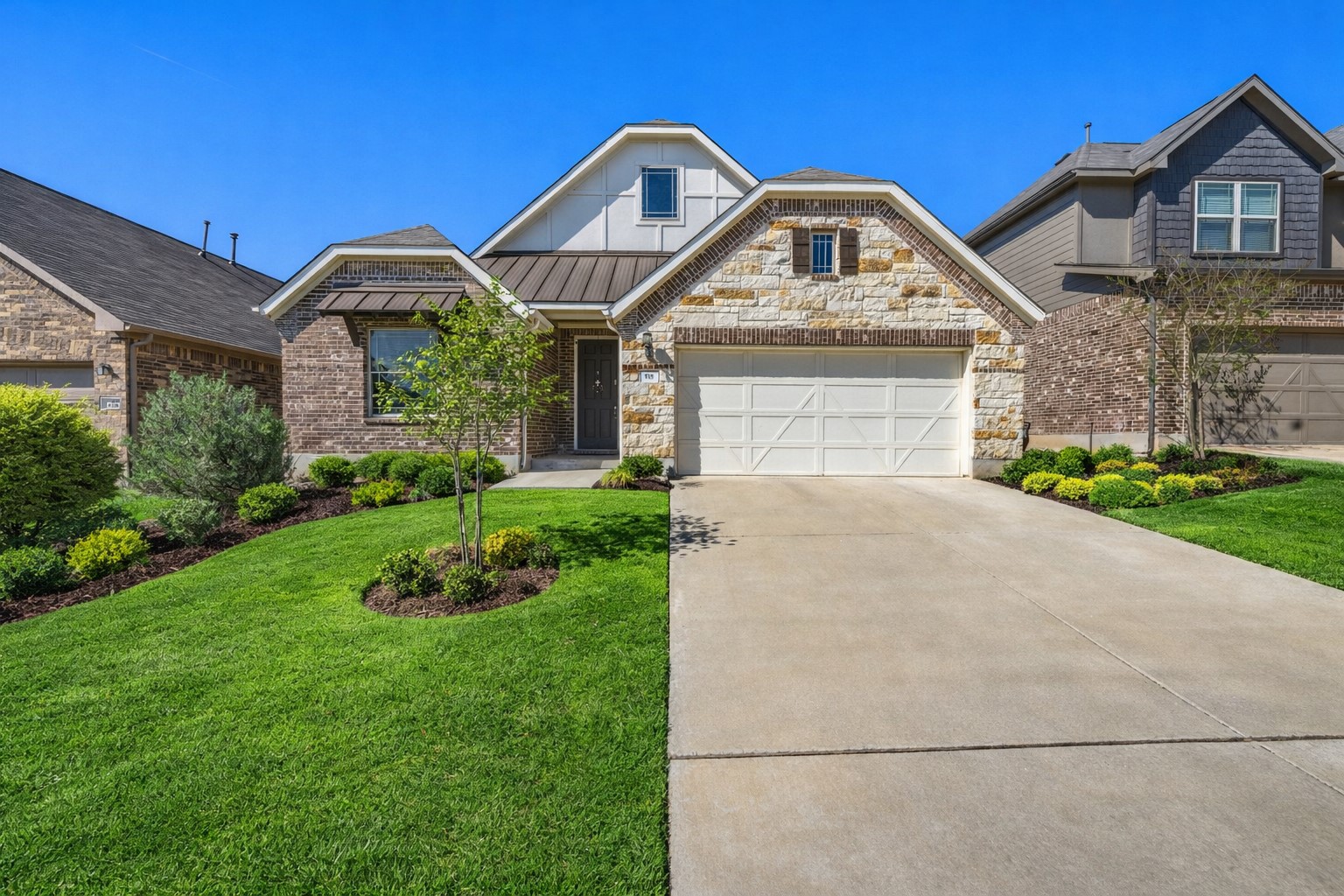 Craftsman-style home with a standing seam roof, driveway, a front lawn, and stone siding