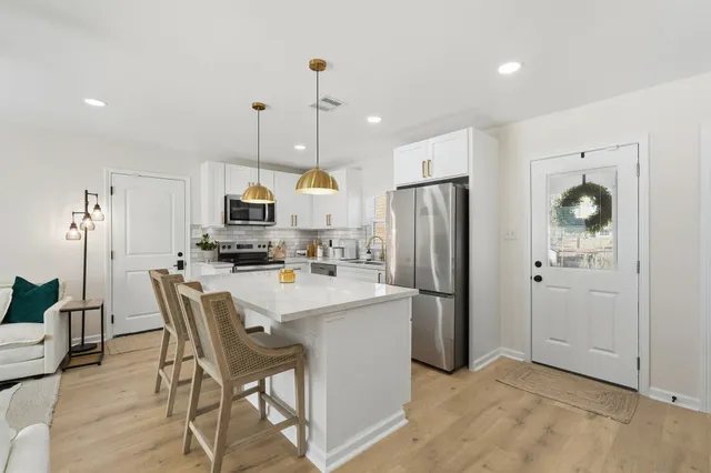 a kitchen with stainless steel appliances a refrigerator a stove a sink dishwasher and a dining table with wooden floor