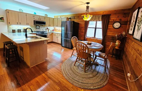 a kitchen with stainless steel appliances granite countertop a stove a refrigerator a kitchen island a dining table and chairs with wooden floor