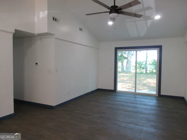 an empty room with wooden floor fan and windows
