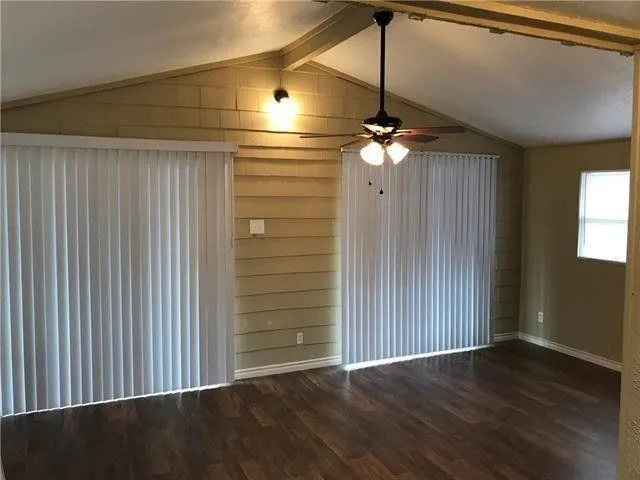 an empty room with wooden floor ceiling fan and window