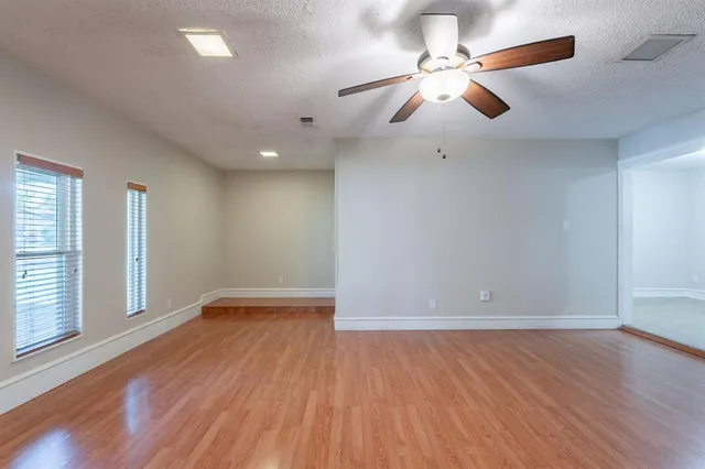 an empty room with wooden floor chandelier fan and windows