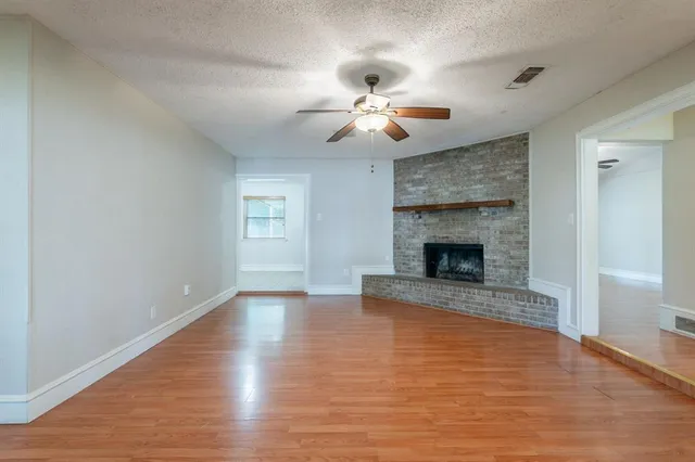 a view of an empty room with wooden floor fireplace and a window