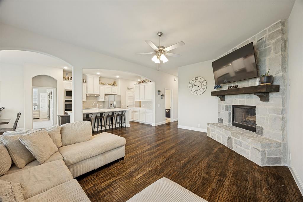 8795 County Road 502 Blue Ridge, TX 75424 - Photo 6 of 33 Spacious living area featuring a stone-clad fireplace with a substantial wood mantel, wood-finish flooring, multiple large windows with blinds, and a ceiling fan