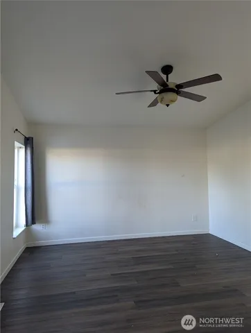 a view of an empty room with wooden floor and a ceiling fan