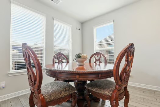 24714 Longwood Forest Drive Spring, TX 77373 - Photo 6 of 21 This dining area features a round wooden table with intricately carved chairs, set against a backdrop of three large windows that allow for plenty of natural light. The bright, neutral walls and tiled floor create an inviting and elegant space.