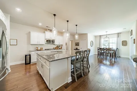 a kitchen with stainless steel appliances granite countertop a stove top oven a refrigerator a dining table and chairs with wooden floor