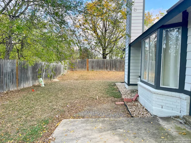 a view of a backyard with large trees and wooden fence