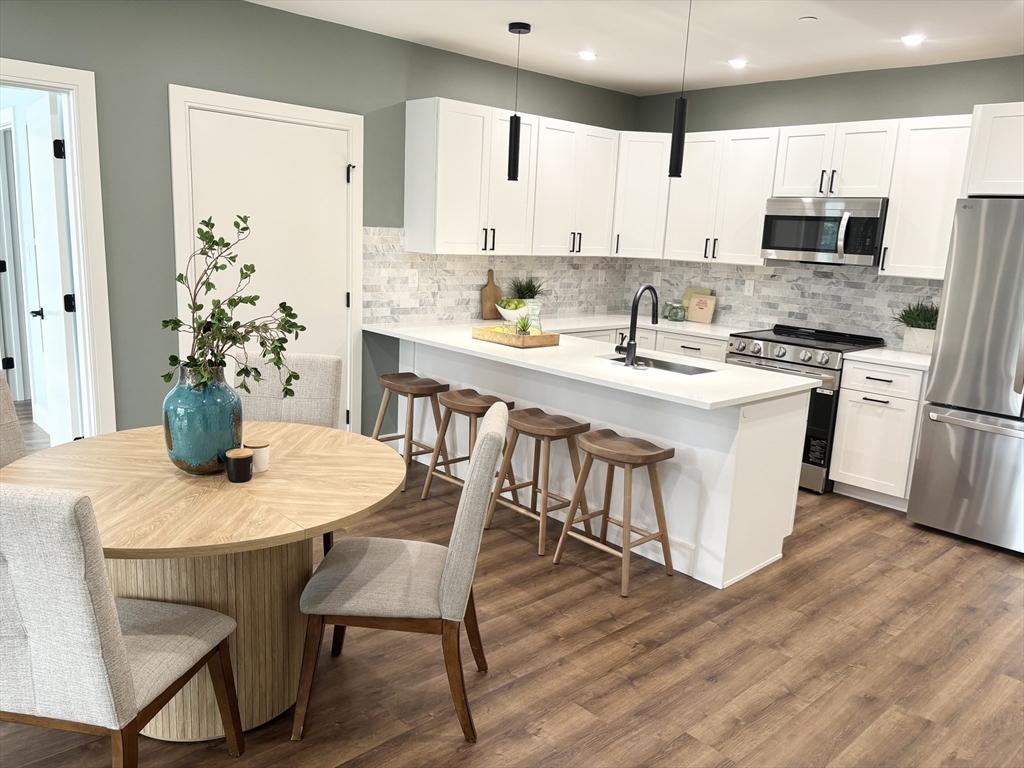 1391 Main Street, Unit 301 Walpole, MA 02081 - Photo 5 of 22 a kitchen with stainless steel appliances granite countertop a dining table chairs refrigerator sink and cabinets