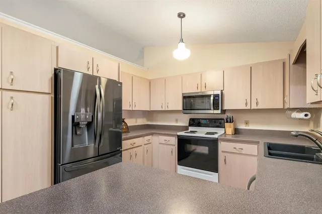 a kitchen with granite countertop a refrigerator a sink a stove and white cabinets