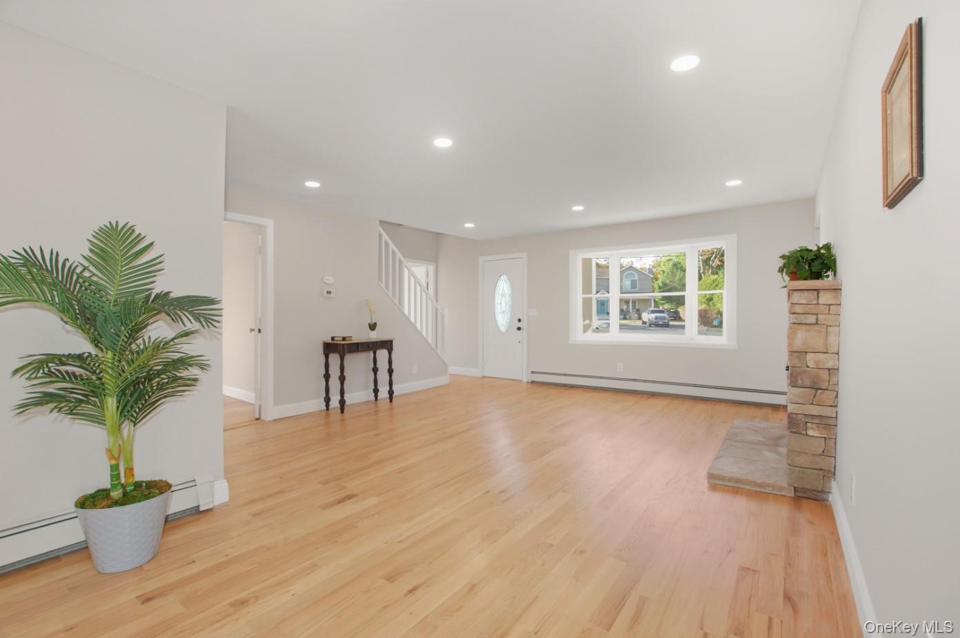 225 Lyman Road East Patchogue, NY 11772 - Photo 2 of 18 Unfurnished living room with light wood finished floors, baseboard heating, recessed lighting, stairway, and a baseboard radiator