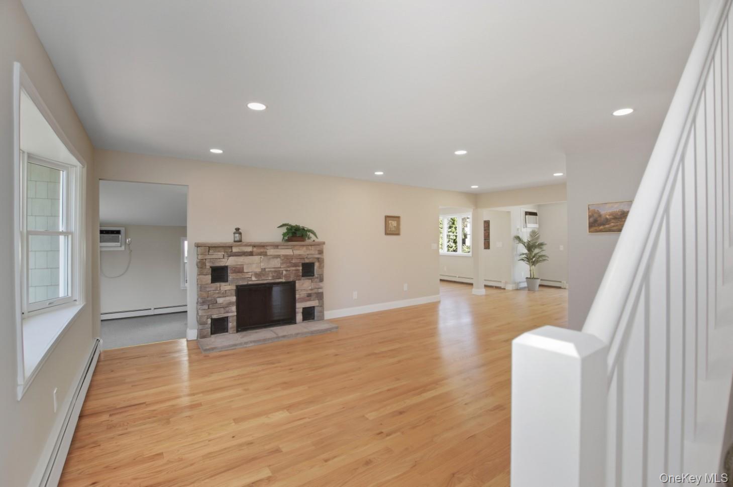 225 Lyman Road East Patchogue, NY 11772 - Photo 5 of 18 Unfurnished living room featuring baseboard heating, a stone fireplace, recessed lighting, light wood-type flooring, and a wall mounted AC