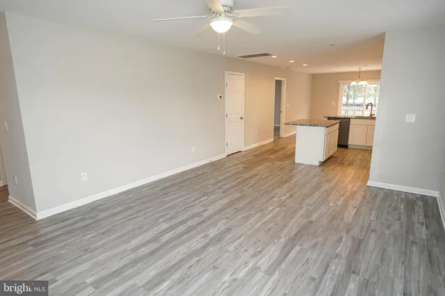 a view of an empty room with wooden floor and a kitchen