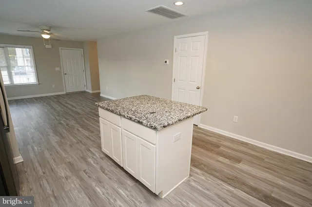 an empty room with wooden floor and kitchen view