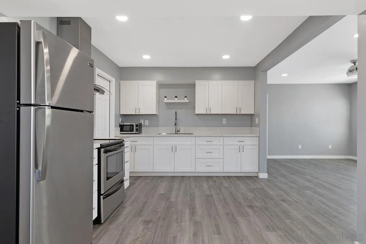 6357 Streamview Drive San Diego, CA 92115 - Photo 6 of 13 a kitchen with granite countertop a refrigerator stove and white cabinets with wooden floor