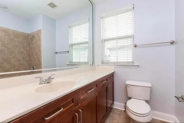a bathroom with a granite countertop toilet a sink a large mirror and a window