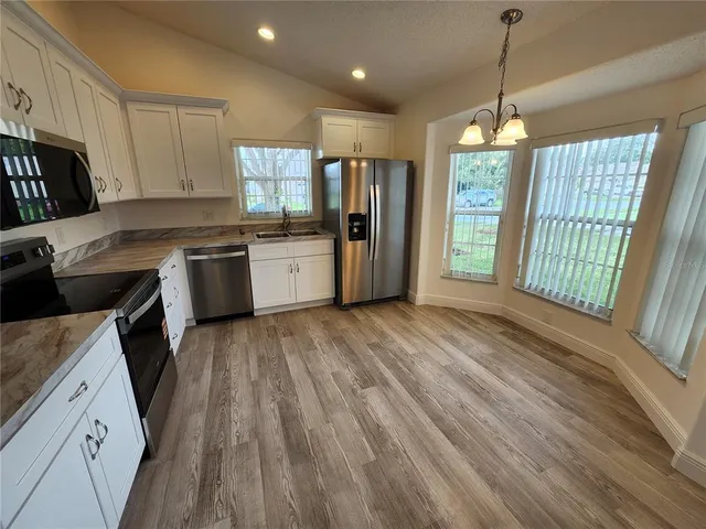 a kitchen with stainless steel appliances granite countertop a refrigerator a sink dishwasher a stove and white countertops with wooden floor