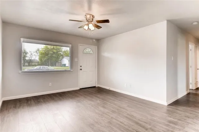 an empty room with wooden floor chandelier fan and windows