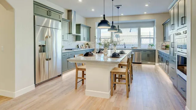 a kitchen with stainless steel appliances granite countertop a refrigerator a sink dishwasher a stove and a dining table with wooden floor