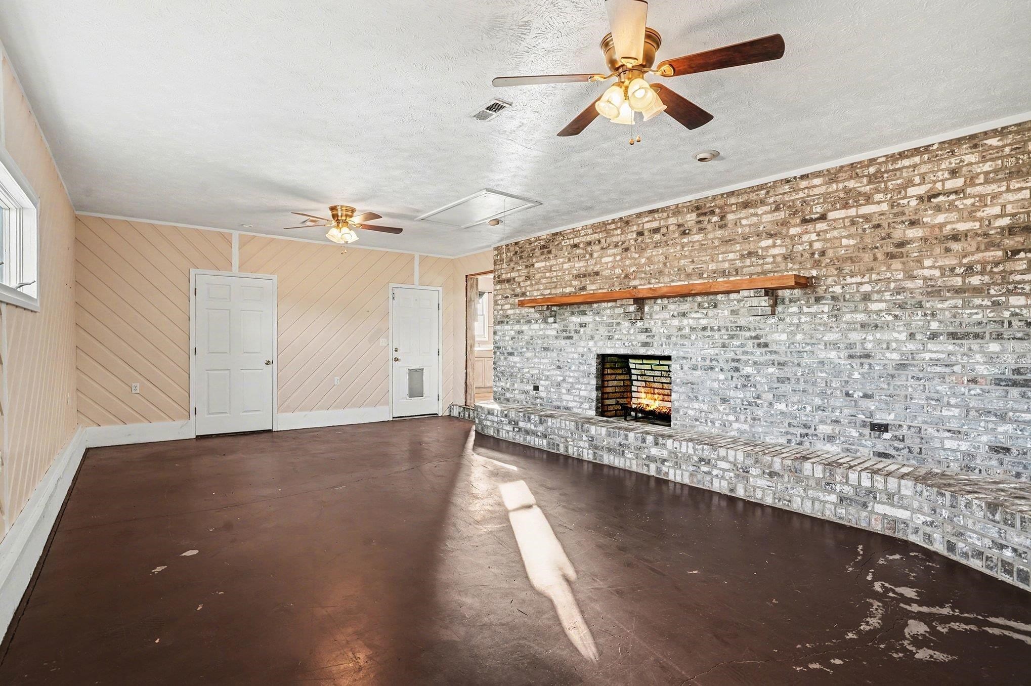 1897 Heritage Road Loris, SC 29569 - Photo 4 of 32 Unfurnished living room featuring ceiling fan, concrete flooring, wood walls, a brick fireplace, and a textured ceiling