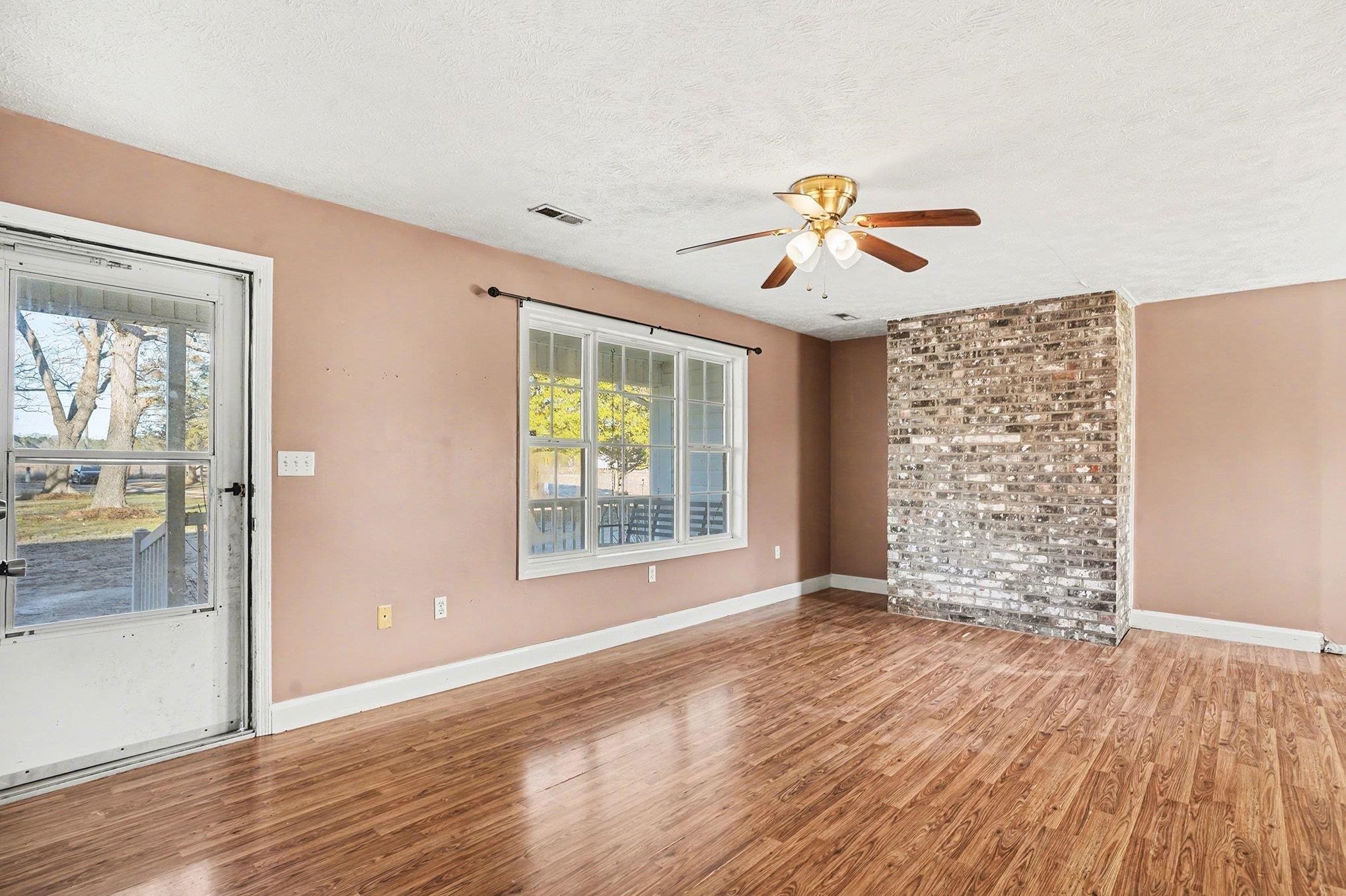 1897 Heritage Road Loris, SC 29569 - Photo 6 of 32 Unfurnished living room with a ceiling fan, a textured ceiling, wood walls, attic access, and a brick fireplace