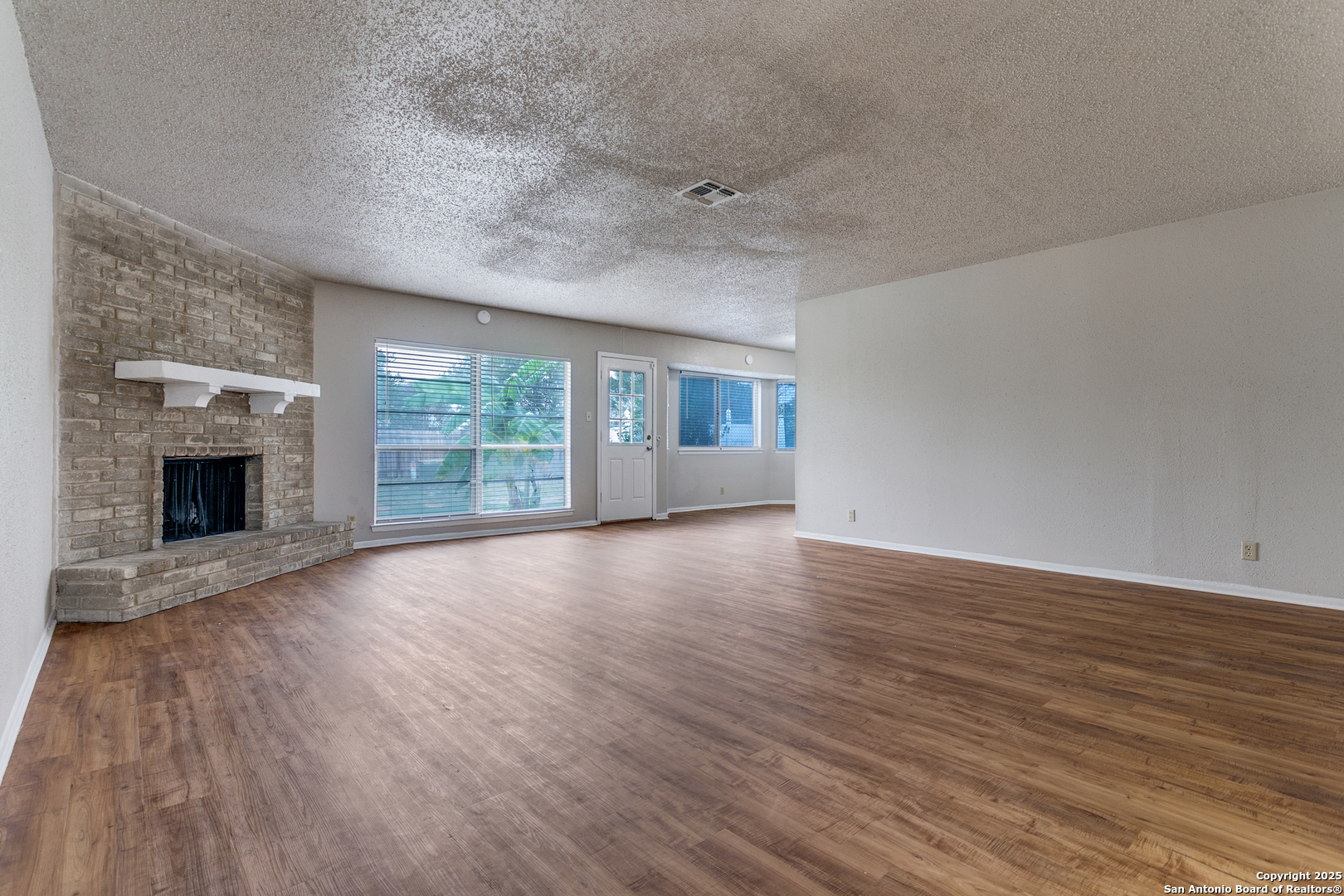 2803 Fred Haise Drive Kirby, TX 78219 - Photo 8 of 24 an empty room with wooden floor fireplace and windows
