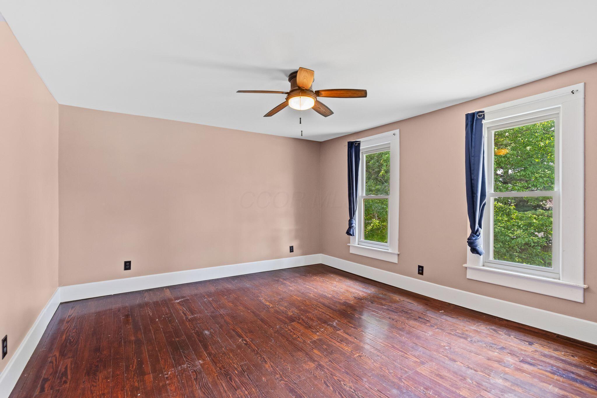 107 Price Road Columbus, OH 43230 - Photo 29 of 51 Spacious room featuring wood-finish flooring, two large windows with white trim, a ceiling fan with integrated lighting, and neutral wall paint
