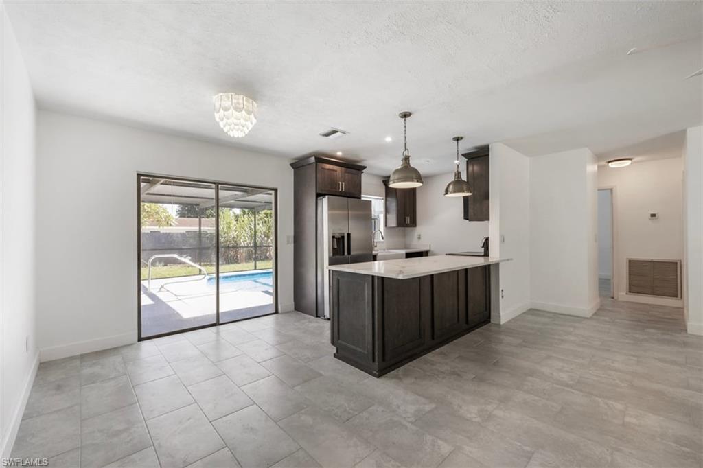 1948 46th Street Southwest Naples, FL 34116 - Photo 11 of 42 Kitchen featuring dark brown cabinetry, hanging light fixtures, light stone countertops, a peninsula, and stainless steel fridge
