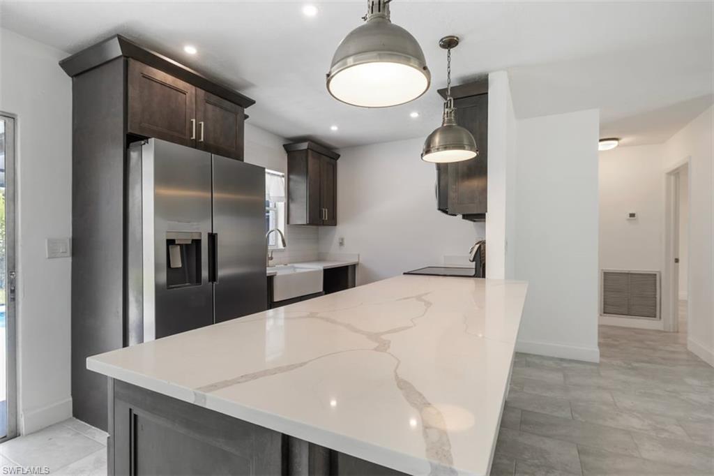 1948 46th Street Southwest Naples, FL 34116 - Photo 6 of 42 Kitchen with stainless steel fridge with ice dispenser, light stone counters, a peninsula, dark brown cabinets, and light tile patterned flooring