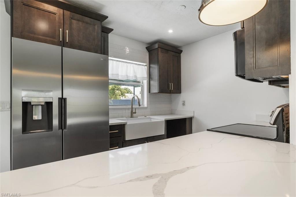 1948 46th Street Southwest Naples, FL 34116 - Photo 7 of 42 Kitchen featuring stainless steel fridge, light stone counters, black range oven, dark brown cabinetry, and tasteful backsplash