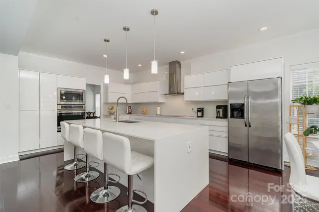 a kitchen with stainless steel appliances kitchen island granite countertop a refrigerator oven a sink a stove and white cabinets with wooden floor