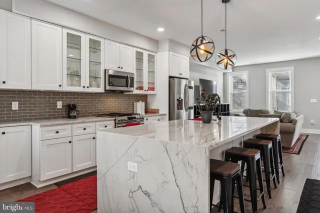 a kitchen with stainless steel appliances granite countertop a stove a sink a refrigerator a microwave a dining table and chairs with wooden floor