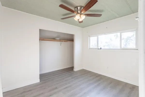 an empty room with wooden floor ceiling fan and windows