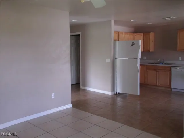 an empty room with wooden floor kitchen view and a window