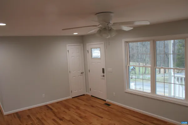 an empty room with wooden floor fan and windows
