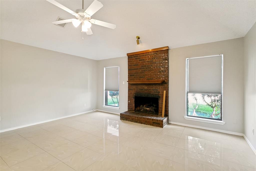 1712 East Peters Colony Road Carrollton, TX 75007 - Photo 11 of 25 Living area featuring a brick fireplace with a wood mantle, two windows with roller shades, light-toned tile flooring, and a ceiling fan