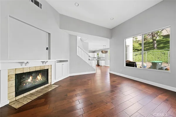 a view of an empty room with wooden floor fireplace and a window