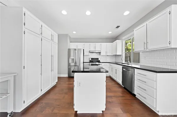 a large kitchen with stainless steel appliances granite countertop a large counter top a sink a stove a refrigerator and cabinets