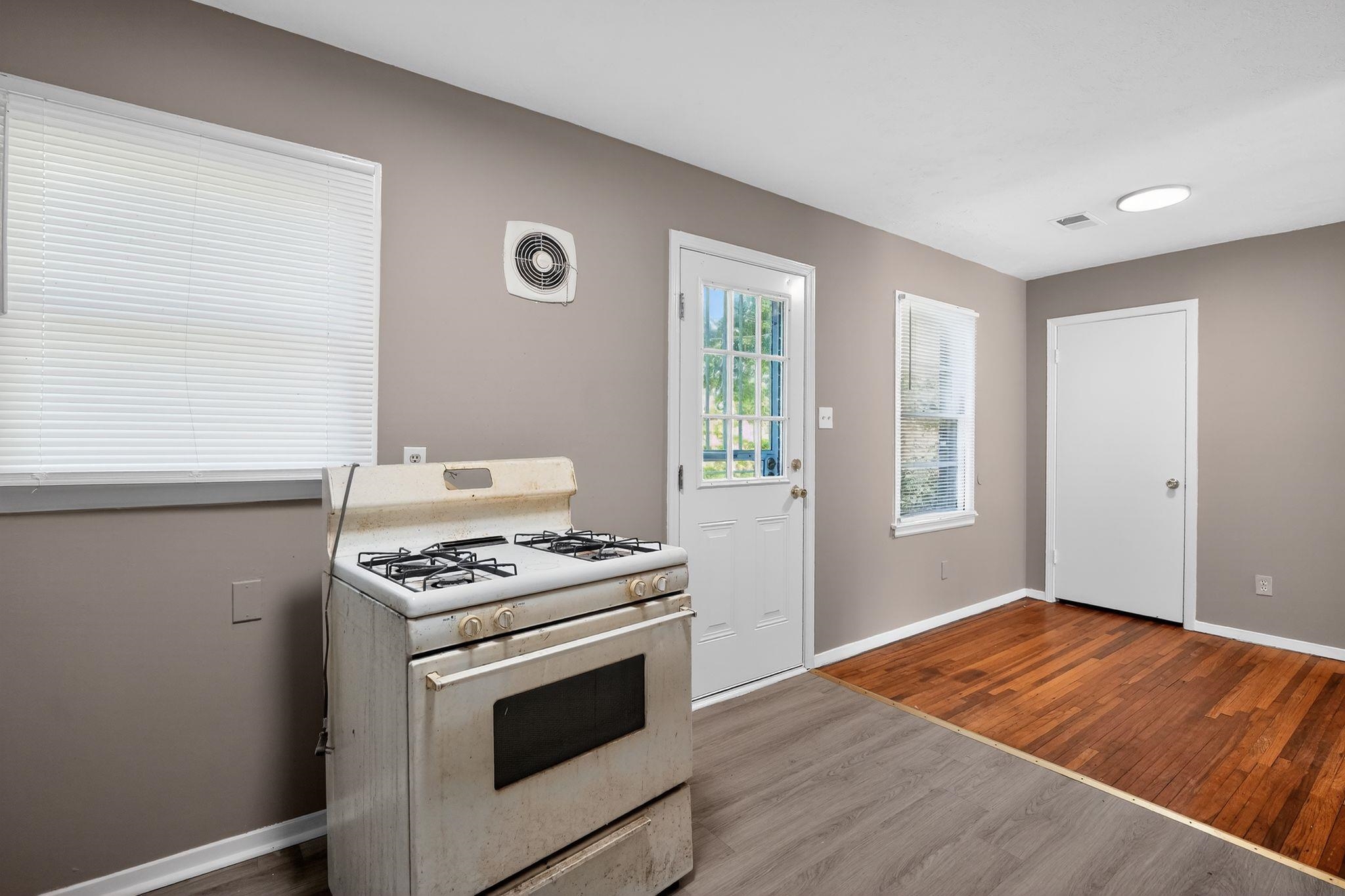 4955 Stacey Road Memphis, TN 38109 - Photo 23 of 35 Interior space featuring a white gas range, two distinct flooring types, an exterior door with multiple glass panes, a round flush-mount ceiling light fixture, and two windows