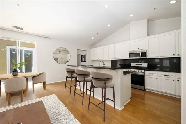 a kitchen with stainless steel appliances kitchen island granite countertop a stove a sink a dining table and chairs with wooden floor