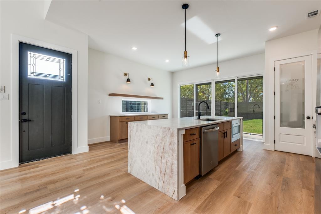 2424 Jeffries Street Dallas, TX 75215 - Photo 16 of 28 Kitchen with light stone counters, open shelves, light wood-style floors, decorative light fixtures, and a center island with sink