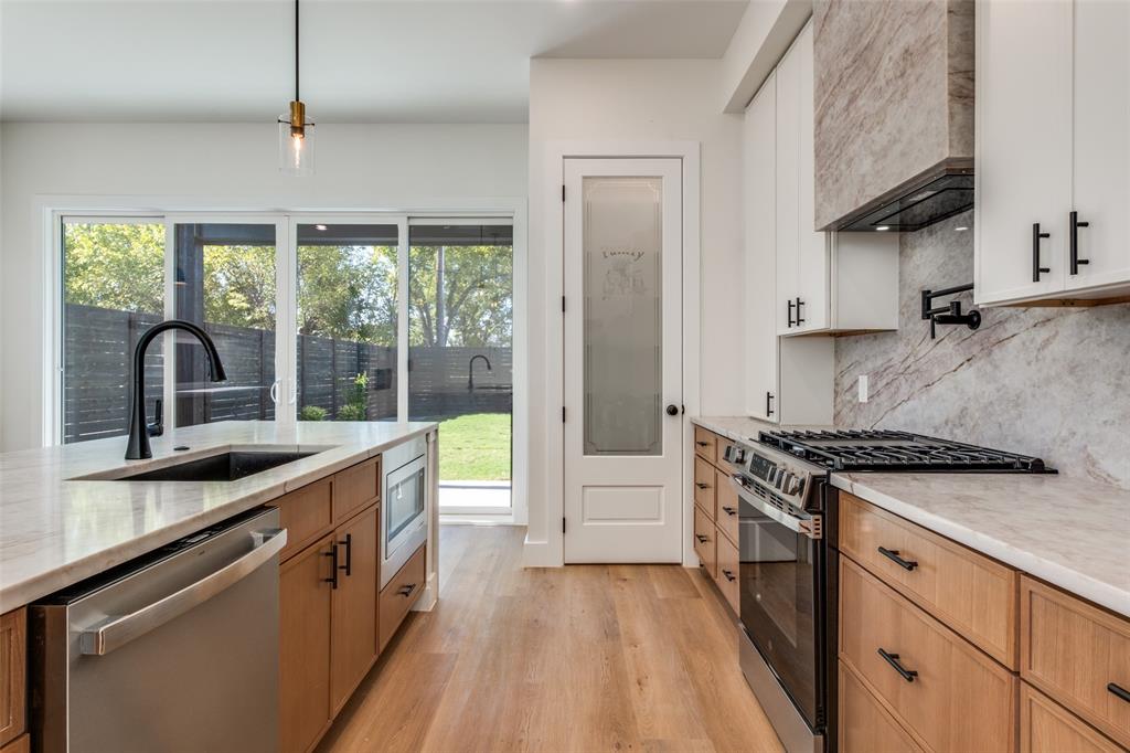 2424 Jeffries Street Dallas, TX 75215 - Photo 18 of 28 Kitchen featuring appliances with stainless steel finishes, pendant lighting, light stone counters, light wood-style floors, and tasteful backsplash